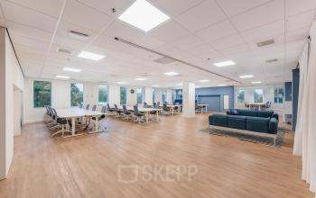 Ruim en licht zakelijk interieur op Koningin Wilhelminaplein 1, Amsterdam Nieuw-West, voorzien van moderne werkplekken en blauwe banken. Een aantrekkelijke optie voor wie een kantoorruimte wil huren.