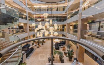 Moderne kantoorruimte in Amsterdam Nieuw-West met centraal atrium, verlichte designlampen en zitgelegenheid. Mensen werken geconcentreerd aan tafels op de begane grond.