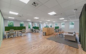 Moderne kantoorpand met open vloerplan op Koningin Wilhelminaplein 1 in Amsterdam Nieuw-West, ideale plek om kantoorruimte te huren, met werkstations, zitgedeelte, en grote ramen voor veel natuurlijk licht.