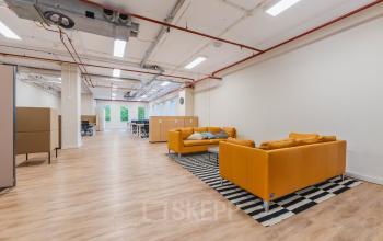 Ruime kantoorruimte aan het Koningin Wilhelminaplein 1, Amsterdam Nieuw-West, met moderne inrichting, houten vloeren en comfortabele zithoeken. De ruimte biedt een inspirerende omgeving voor werken en vergaderen.