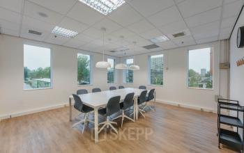 Vergaderruimte op Koningin Wilhelminaplein 1 in Amsterdam Nieuw-West, met grote tafel en stoelen, ideaal voor kantoor. Ruime ramen bieden uitzicht en veel licht, geschikt voor zakelijke bijeenkomsten.