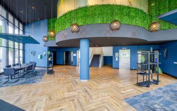 Kantoorruimte huren bij Overschiestraat 61, Amsterdam Nieuw-West. Moderne gemeubileerde lobby met blauwe muren, groene plantenwand, en lounge zithoekjes. 