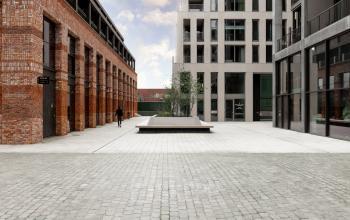 Buitenaanzicht van een modern kantoorpand op Papaverhof 58 in Amsterdam Noord, met elegante bakstenen en glasconstructie. Een enkele persoon loopt over het plein voor het gebouw.