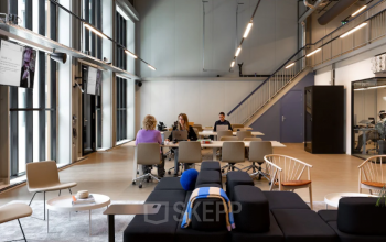 Kantoorruimte huren aan Papaverhof 58, Amsterdam Noord met moderne werkplekken en grote ramen. Verschillende mensen zijn bezig met zakelijke activiteiten aan tafels.