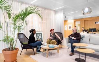 Drie mensen in een ontspannen gesprek in een modern kantoorpand in Amsterdam Noord, gelegen aan Mt. Lincolnweg 38-40. De ruimte is stijlvol ingericht met comfortabele stoelen en een grote plant.