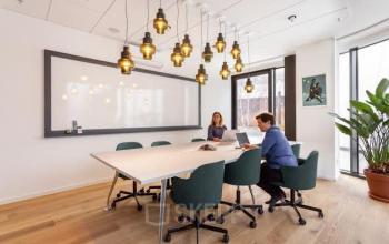 Een moderne vergaderruimte in een kantoorpand aan de Mt. Lincolnweg 38-40, Amsterdam Noord. Twee mensen zitten aan een tafel tijdens een zakelijke bijeenkomst.