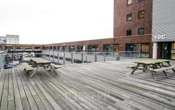 Modern kantoorpand op Asterweg 19, Amsterdam Noord, met houten terras en picknicktafels voor zakelijke ontspanning of informele meetings.