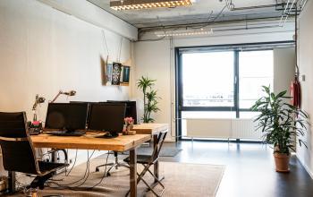 Moderne, goed verlichte kantoorruimte met houten bureau, computers en planten, gelegen in het kantoorpand aan Asterweg 19 in Amsterdam Noord.