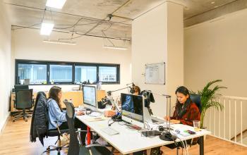 Moderne, lichte kantoorruimte met werkende mensen aan bureaus met computers en aantekeningen op Asterweg 19 in Amsterdam Noord.