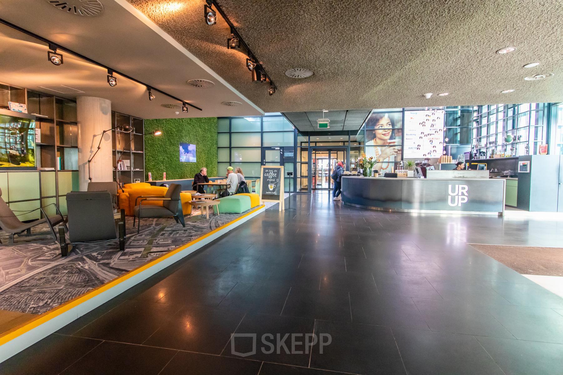 Ruime entree van een kantoorpand op Piet Heinkade 55 in Amsterdam Oost, met moderne receptie en comfortabele zitgelegenheden. Twee personen voeren een gesprek aan een tafel. Kantoorruimte huren nabij voorzieningen.