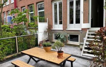 Rustige buitenruimte van een kantoorpand op Domselaerstraat 27 in Amsterdam Oost met een picknicktafel, groene planten en rijtjeshuizen op de achtergrond, ideaal voor een pauze of informele vergadering.