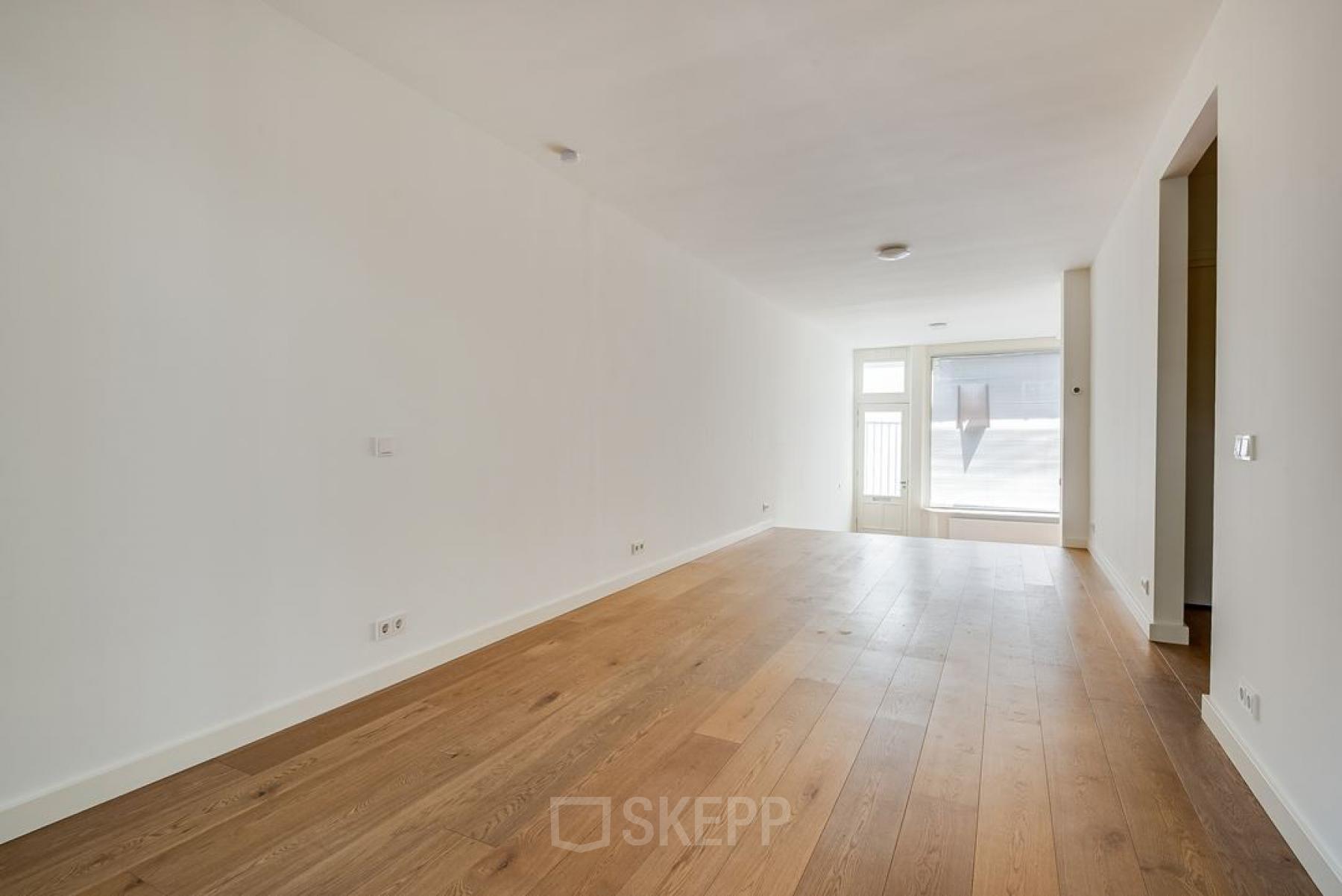 Lichte kantoorruimte aan de Domselaerstraat 27 in Amsterdam Oost, klaar voor huur en inrichting. De ruimte biedt een houten vloer en een groot raam voor natuurlijk licht.