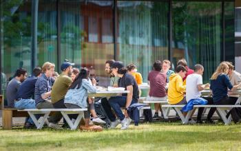 Groep mensen in zakelijke omgeving buiten bij het kantoorpand op Science Park 301, Amsterdam Oost, kantooruimte huren. Gezellig gesprekken aan picknicktafels bij glazen gevel.