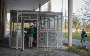 Fietsenstalling bij kantoorpand Science Park 301 in Amsterdam Oost. Een persoon in groene jas parkeert zijn fiets in de beveiligde stalling naast het moderne kantoor.