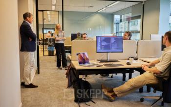 Moderne kantoorruimte op Science Park 301 in Amsterdam Oost met collega's in overleg. De ruimte beschikt over werkplekken met computerschermen, ergonomische meubels en veel natuurlijk licht, ideaal voor samenwerken en creatieve projecten.