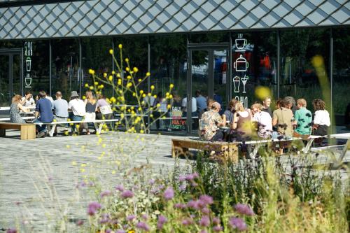 Buiten het kantoorpand op Science Park 301 in Amsterdam Oost zitten mensen aan picknicktafels. De uitstraling is modern en uitnodigend, perfect voor informele ontmoetingen of een ontspannen kantooromgeving.