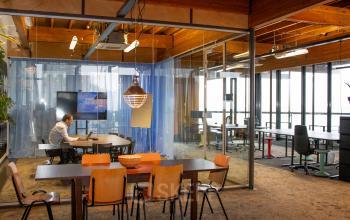 Kantoorruimte huren op KNSM-Laan 171 in Amsterdam Oost met stijlvolle inrichting en helder daglicht. Een persoon werkt aan een laptop in een vergaderruimte.