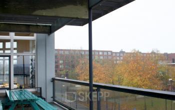 Een kantoorruimte in Amsterdam Oost met uitzicht op de stad, voorzien van een ruim balkon met houten bankjes. Ideaal om een kantoor te huren met een ontspannende buitenruimte.