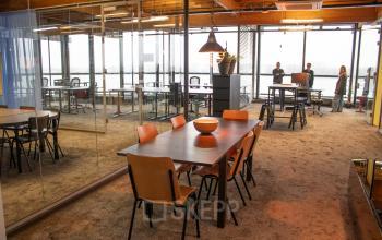 Levendige kantoorruimte op de KNSM-Laan 171, Amsterdam Oost, met een grote vergadertafel en uitzicht op de stad. Personen zijn bezig met gesprekken en taken. Ideaal voor kantoorruimte huren.