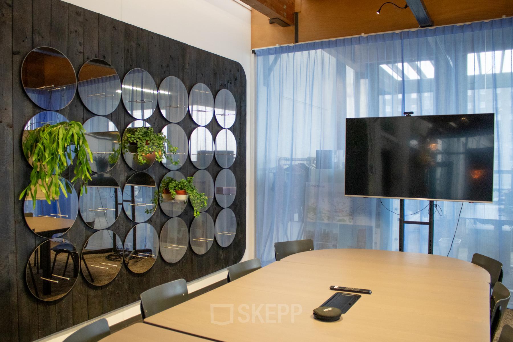 Moderne vergaderruimte op KNSM-Laan 171 in Amsterdam Oost, met een grote tafel, stoelen, planten en een muur met ronde spiegels.
