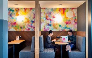 Kantoorruimte huren in Weesperstraat 61, Amsterdam Oost. Twee personen werken aan een tafel in een kleurrijk ingerichte werkruimte met moderne meubels.