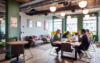 Kantoorruimte huren op Weesperstraat 61 in Amsterdam Oost met lichte open floorplan, groen decor, houten vloer, en mensen die overleggen aan een grote tafel.