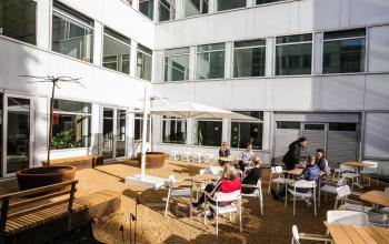 Zakelijke bijeenkomst in buitenruimte bij kantoorpand Apollolaan 151, Amsterdam Oud Zuid, met meerdere personen zittend en converserend aan tafels onder parasols.