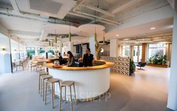 Moderne kantoorruimte op Apollolaan 151 in Amsterdam Oud Zuid met een stijlvolle ronde balie waar medewerkers klanten ontvangen en overleggen. Geschikt voor het huren van professionele werkplekken.