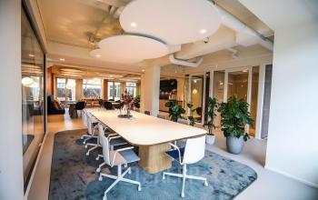 Moderne kantoorruimte op Apollolaan 151 in Amsterdam Oud Zuid met ruime vergadertafel, stijlvolle verlichting en groene planten, ideaal voor huur. Gezellige en inspirerende werkomgeving voor zakelijke activiteiten.