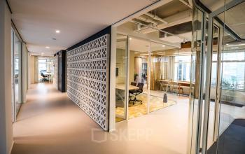 Moderne kantoorruimte huren op Apollolaan 151 in Amsterdam Oud Zuid met glazen wanden, lichte inrichting en uitzicht op open kantoorruimtes, geschikt voor professionele zakelijke activiteiten.