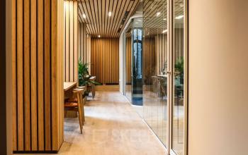 Moderne kantoorruimte op Apollolaan 151 in Amsterdam Oud Zuid met houten wanden, glazen scheidingswanden en twee lege stoelen aan een tafel.