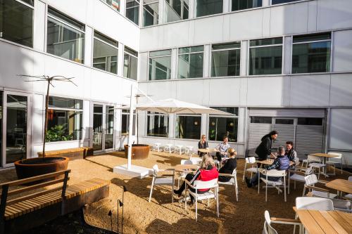 Zakelijke bijeenkomst in buitenruimte bij kantoorpand Apollolaan 151, Amsterdam Oud Zuid, met meerdere personen zittend en converserend aan tafels onder parasols.