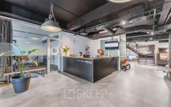 Moderne receptie met balie en ontvangstgedeelte in een kantoorpand op Olympisch Stadion 24-28, Amsterdam Oud Zuid. Een vrouw zit achter de balie en verwelkomt bezoekers.