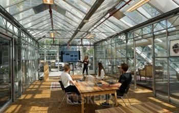 Kantoor met glazen wanden in Amsterdam Riekerpolder, gelegen op Johan Huizingalaan 400. Drie mensen bij vergadertafel, één presenteert aan een scherm. Ruimte biedt een heldere en moderne werkomgeving.