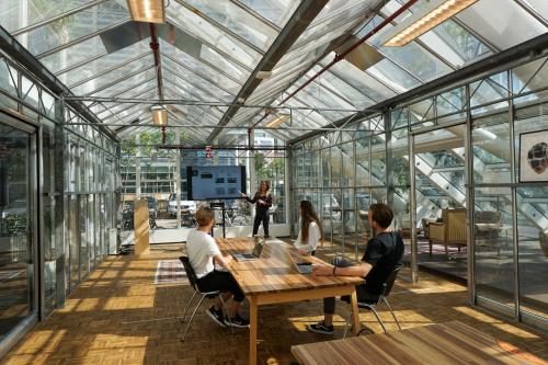 Kantoor met glazen wanden in Amsterdam Riekerpolder, gelegen op Johan Huizingalaan 400. Drie mensen bij vergadertafel, één presenteert aan een scherm. Ruimte biedt een heldere en moderne werkomgeving.