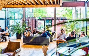 Zakelijke bijeenkomst in lichte en ruime kantoorlounge op John M Keynesplein 12-46, Amsterdam Riekerpolder, met verschillende mensen in gesprek. Ideale plek voor het huren van kantoorruimte in een inspirerende omgeving.