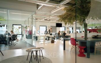 Modern kantoorpand op John M Keynesplein in Amsterdam Riekerpolder met open werkplekken en een glazen wand. Mensen werken geconcentreerd aan bureaus.