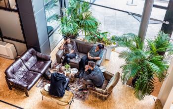 Kantoorruimte te huur op het John M Keynesplein in Amsterdam Riekerpolder, met stijlvolle meubels en groen, waar mensen in gesprek zijn in een sfeervolle lounge.
