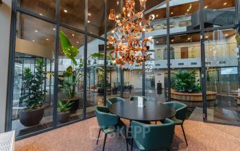 Moderne kantoorruimte op John M. Keynesplein 4-10, Amsterdam Riekerpolder, met een glazen wand, groene planten en een ronde tafel met stoelen voor vergaderingen.