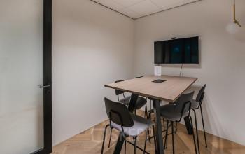 Moderne vergaderruimte in een kantoorpand op John M. Keynesplein 4-10, Amsterdam Riekerpolder, voorzien van een tafel met zes stoelen en een scherm aan de wand voor presentaties.