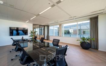 Moderne vergaderruimte met glazen tafel en zwarte stoelen in het kantoorpand op Thomas R. Malthusstraat 1-3, Amsterdam Riekerpolder.