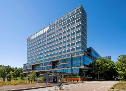 Voorgevel van kantoorpand aan Thomas R. Malthusstraat 1-3, Amsterdam Riekerpolder, met fietsers en voetgangers op de voorgrond.