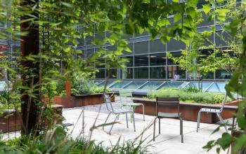Buitenruimte van het kantoorpand op Teleportboulevard 120 in Amsterdam Sloterdijk, met diverse stoelen omgeven door groene planten en kantoorgebouw op de achtergrond.