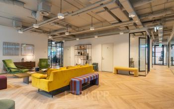 Moderne kantoorruimte huren aan Teleportboulevard 120 in Amsterdam Sloterdijk, met kleurrijke meubels, houten vloer en glazen wanden. De ruimte straalt een open en inspirerende werkomgeving uit.