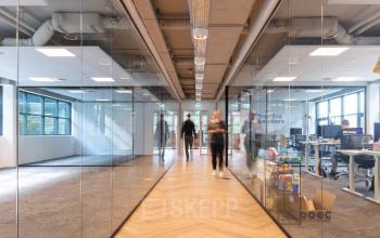 Moderne kantoorruimte huren op Teleportboulevard 120, Amsterdam Sloterdijk, met glazen wanden en loopgang. Zakelijke activiteiten zichtbaar met rondlopende personen.
