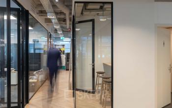 Binnenzicht in het kantoorpand op Teleportboulevard 120, Amsterdam Sloterdijk met moderne glazen wanden en stijlvolle houten vloer. Een persoon wandelt door de gang in een zakelijke setting, ideaal voor kantoorruimte huren.