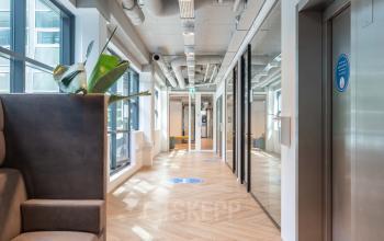 Binnenkant van een kantoorpand op Teleportboulevard 120, Amsterdam Sloterdijk. Moderne open werkruimte met grote ramen, houten vloer en enkele meubels, ideaal voor kantoorruimte huren.