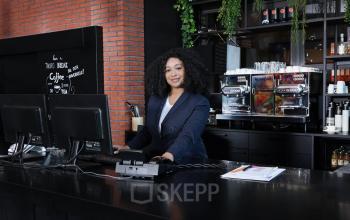 Zakelijke vrouw werkt achter de balie in een stijlvol kantoorpand op Teleportboulevard 110 in Amsterdam Sloterdijk. Op de achtergrond zijn koffiemachines en groene planten zichtbaar.
