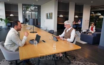 Zakelijke mensen werken in een moderne kantoorruimte met lange houten tafel en comfortabele stoelen in Amsterdam Sloterdijk aan de Teleportboulevard 110.