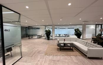 Ruime open kantoorruimte te huur in Amsterdam Sloterdijk, modern ingericht met glazen wanden en een grote witte bank. Planten en stijlvol meubilair creëren een uitnodigende sfeer voor productief werken.